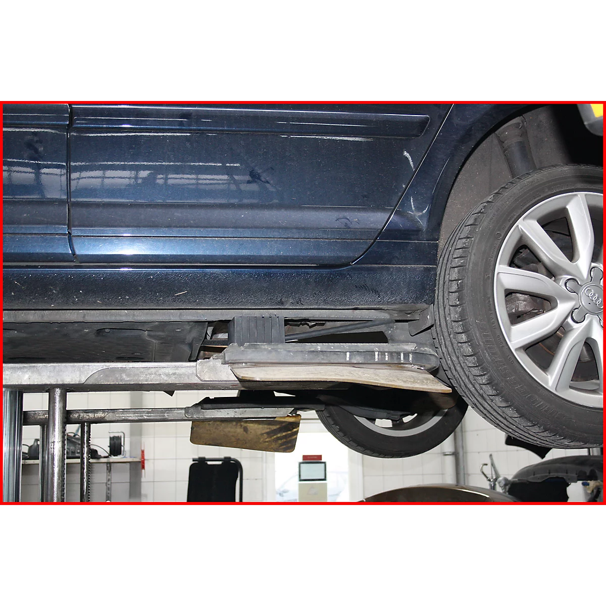 Dunkelblaues Auto auf Hebebühne, Blick auf Reifen und Unterboden. Werkstatt-Umgebung mit Hebevorrichtung.